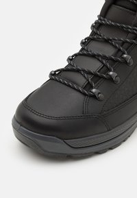 Schwarzer Outdoor-Stiefel mit glattem Lederobermaterial, strukturierten Akzenten, Gummisohle und schwarz-weißen Schnürsenkeln, die durch Kunststoffösen gefädelt sind.