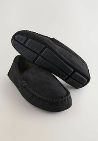 Sorte ruskinds moccasin tøfler med flettet detaljering, blød tekstur og gummitrækkraftsåler. Indvendigt har de et ternet mønster.
