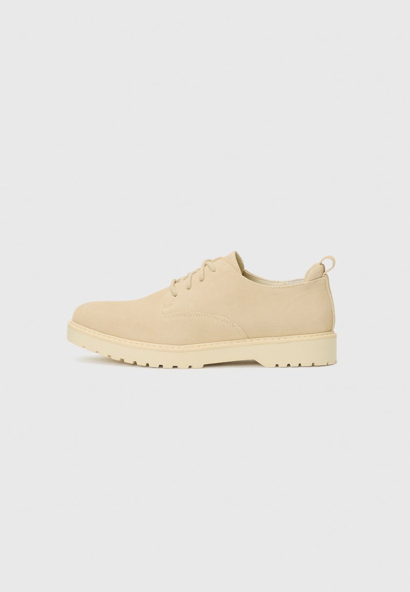 Beige suede lace-up shoes with a rounded toe, textured surface, and a chunky white rubber sole featuring a tread pattern.