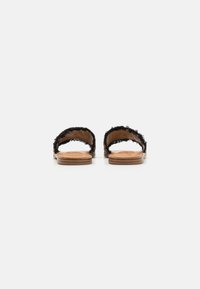 Svarta tygslip-onsandaler med fransad textur, platt träsohle och minimalistisk design, som visar bakvyn och öppen häl.