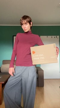 Top de mangas longas em bordeaux combinado com calças cinzas de perna larga. Modelo segura uma caixa da Zalando em castanho claro com o texto: "Ama-me. Usa-me."