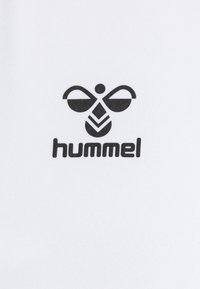 Tissu blanc avec un logo Hummel noir, qui comprend des formes stylisées : deux lignes courbées au-dessus et un design géométrique en dessous.