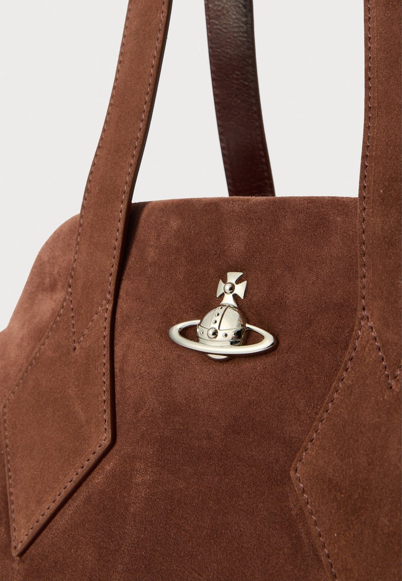 Bolso de ante marrón con un diseño estructurado, que presenta un charm metálico con temática espacial como un acento notable y correas de cuero resistentes.