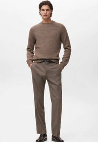 Jersey marrón de punto con cuello redondo, combinado con pantalones rectos en un marrón claro. El modelo lleva botas de cuero marrón oscuro.