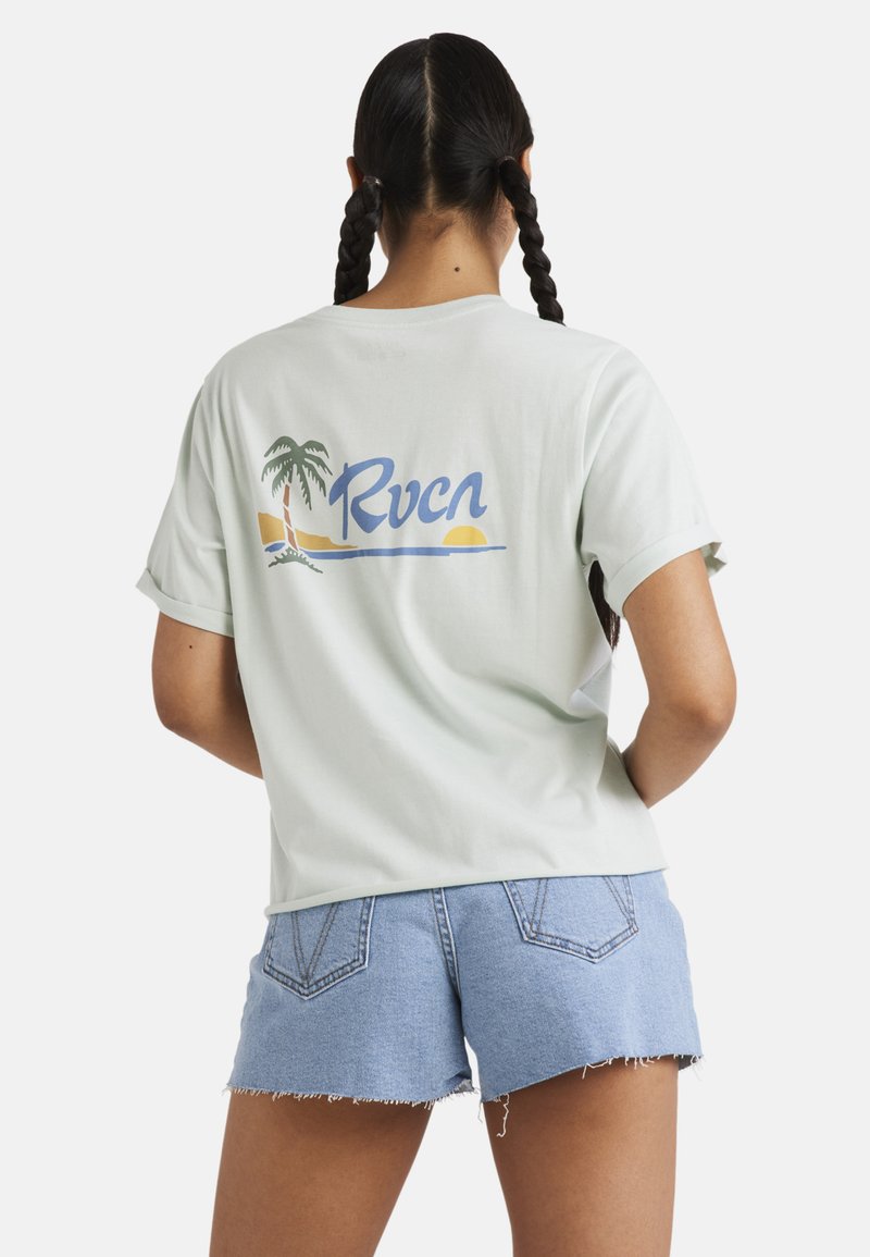 Světle zelené tričko s krátkým rukávem, na kterém je grafika palmového stromu a logo "Rvca" na zadní straně, v kombinaci se svetle modrými denimovými šortkami.