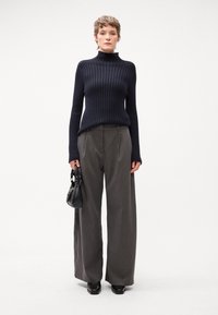 Jūras spēku ribota turtlenecka sega apvienota ar augsto vidukli, plašajām pelēkajām svītrainajām biksēm. Modelis tur nelielu melnu rokassomiņu.