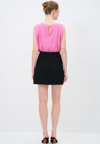 Roze mouwloze top met een keyhole achterkant, gecombineerd met een zwarte minirok. Gladde stof met een rechte snit. Model draagt zwarte hoge hakken.