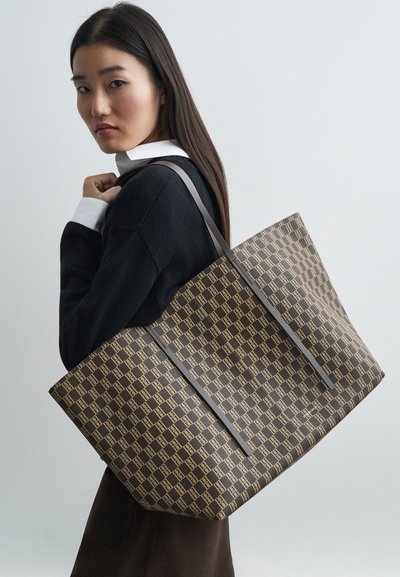 Brown patterned tote bag with light brown accents and long gray straps, featuring a rectangular shape and textured surface.