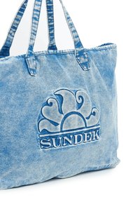 Borsa tote in denim di tonalità blu, con un logo del sole in rilievo e la parola "SUNDEK". La borsa ha robuste maniglie in tessuto blu.