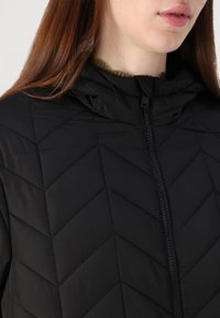 Black puffer jacket featuring a chevron quilted design, high collar, and front zipper closure. Material appears smooth and lightweight.