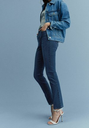 Džínová bunda v světlé modré, přiléhavý šedý top, tmavě modré úzké džíny a bílé sandály na podpatku. Hladká textura a klasický design po celém kousku.