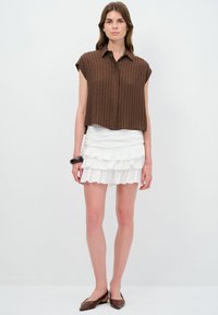 Blusa marrone a righe con maniche corte e colletto; abbinata a una minigonna bianca a strati con volant. Ballerine marroni completano l'outfit.