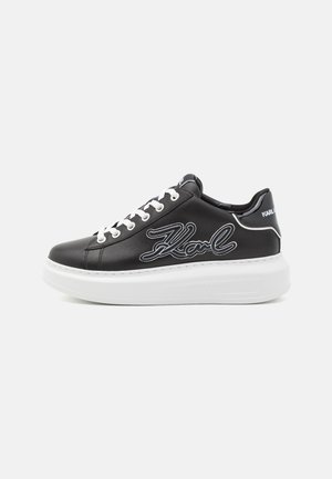 Baskets en cuir noir avec semelle en caoutchouc blanche, dotées de lacets et du logo "Karl" en blanc sur le côté. Texture lisse avec un design épuré.