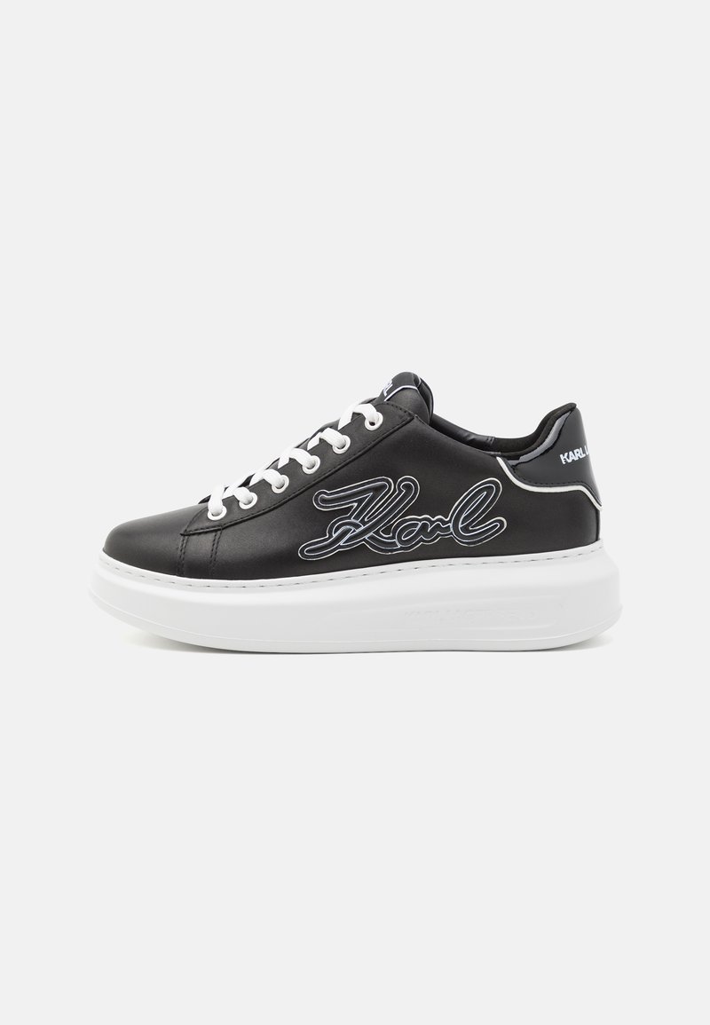 Zapatillas de cuero negro con suela de goma blanca, que presentan cordones y el logo "Karl" en blanco en el costado. Textura suave con un diseño elegante.