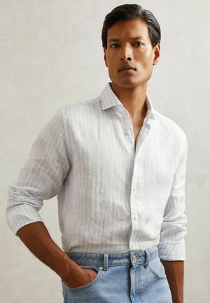 Fehér gombos ing világoskék csíkokkal, felhajtott hosszú ujjakkal, magas derekú világoskék farmernadrággal párosítva. Sima szövettextúra.