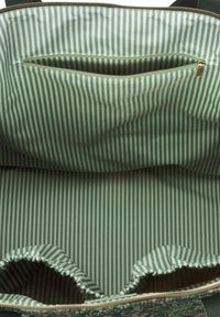Groene stoffen draagtas, met een gestreepte groene binnenkant, een ritsvak en gathered randen aan de basis voor extra textuur.
