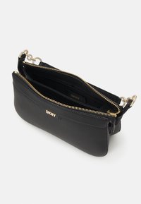 Fekete bőrtáska keresztpántos kialakítással, arany színű kiegészítőkkel, dupla cipzáras rekeszekkel, és DKNY logó részletezéssel. Simább textúra, karcsú dizájn.