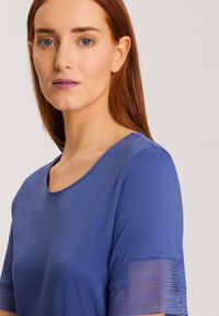Top blu con scollo rotondo e maniche corte; le maniche presentano un dettaglio testurizzato. Tessuto liscio, morbido al tatto e design semplice.