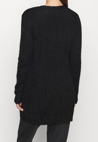 Svart lång tröja med en texturerad, fluffig stickning, rund halsringning och förlängda ärmar, med en längre baksida för ökad täckning.