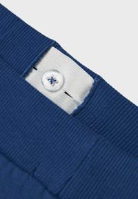 Marineblauer Rippstoffbund mit einem weißen Innenfutter. Verfügt über einen transparenten Knopf mit blauen Akzenten und sauberen Stichtdetails.