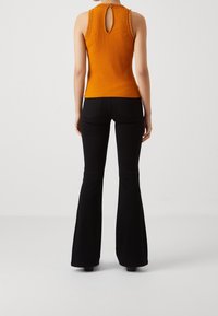 Orange ribbad linne med nyckelhålsrygg, i kombination med svarta utsvängda byxor. Linnet har flätade detaljer på axlarna.