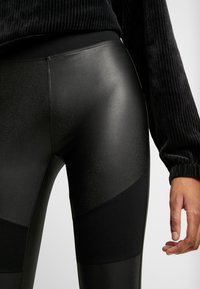 Zwarte leggings met een glanzende afwerking en matte paneelaccenten. Beschikt over een brede tailleband en een aansluitend ontwerp voor comfort en flexibiliteit.