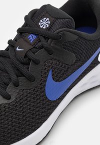 Chaussure de sport noire avec dessus en mesh, présentant un logo Nike bleu et des accents assortis. Design arrondi, lacets noirs et semelle blanche rembourrée.