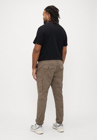 Μαύρο μπλουζάκι με μπεζ παντελόνι cargo που έχει τσέπες, στενές μανσέτες και γκρι αθλητικά παπούτσια. Ουδέτερο φόντο.