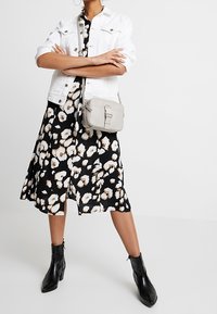 Czarna sukienka w biały kwiatowy wzór, zestawiona z białą dżinsową kurtką, szarym torebką na ramię i czarnymi botkami za kostkę.