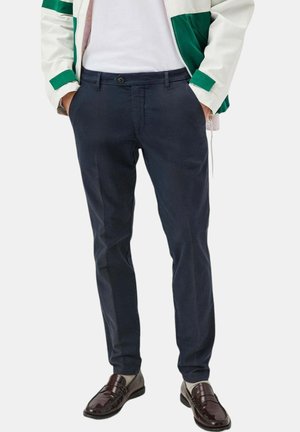 Chino blu navy con vestibilità slim e tasche anteriori, dotati di chiusura a bottone e una leggera texture. Abbinati a scarpe scure e lucide.