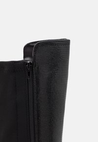 Botte noire avec une tige synthétique texturée et une fermeture éclair sur le côté. Doublure en tissu lisse, silhouette élégante et détail subtil de motif reptile.