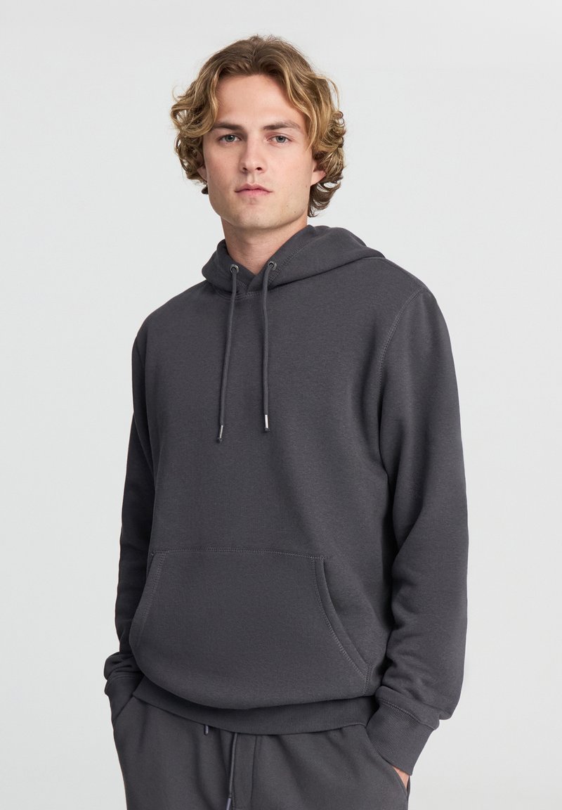 Felpa con cappuccio grigia realizzata in tessuto morbido; presenta una tasca frontale e stringhe regolabili. Le rifiniture includono polsini e orlo a costine.