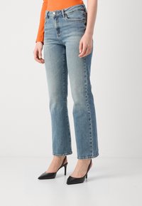 Jeans azzurri chiari a gamba dritta con vita alta, dotati di chiusura a bottone e tasche frontali, abbinati a décolleté nere con punta appuntita.