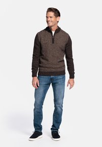 Donkerbruine gebreide pullover met een ritskraag, voorzien van een gestructureerd patroon; gedragen met slim-fit blauwe jeans en zwarte schoenen.