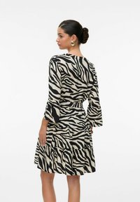 Vestido de estampado cebra en negro y beige con mangas largas acampanadas, cintura ceñida y falda de niveles, confeccionado en una tela ligera.