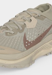 Μπεζ αθλητικό παπούτσι Nike για τρέξιμο με αναπνεύσιμο άνω μέρος από δίχτυ, μπεζ κορδόνια, ροζ σήμα και σόλα Zoom Air σχεδιασμένη για τρέξιμο σε μονοπάτια.