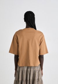 Brun bomulls t-skjorte med korte ermer og avslappet passform. Designet har en ren halslinje og rett kant, kombinert med et rutet lagdelt skjørt.
