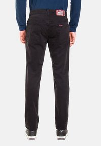 Pantaloni neri in cotone con taglio a gamba dritta, dotati di tasche posteriori e etichetta con marchio sulla vita. Indossati con sneakers nere.