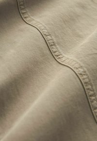 Gros plan d'un tissu beige avec des coutures détaillées le long d'une couture courbe, montrant la texture et le tissage du tissu.