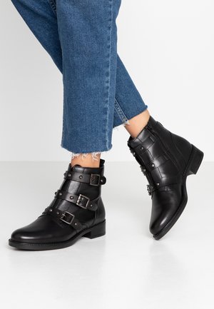 Bottes noires en cuir jusqu'à la cheville avec plusieurs boucles en métal, un petit talon carré et des accents texturés. Couture visible et détail de fermeture éclair sur le côté.