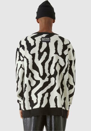 Maglione a righe in bianco e nero realizzato in tessuto a maglia, con design astratto, maniche lunghe e scollo rotondo, dotato di un'etichetta sul retro.
