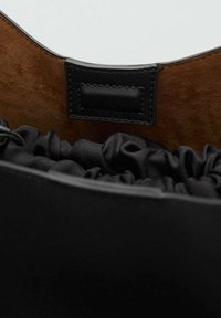 Interno della borsa nera caratterizzato da materiale in raso arricciato, un accento in pelle nera liscia e un rivestimento scuro e testurizzato. Linguetta di chiusura visibile.