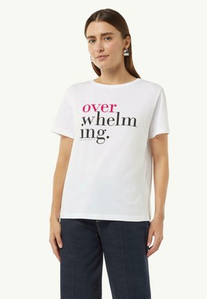 Biała bawełniana koszulka z krótkim rękawem i okrągłym dekoltem, z wyrazem "przytłaczający" w odważnej czarno-różowej typografii. Granatowe dżinsy.