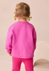 Fuchsia Sweatshirt mit überschnittenen Schultern und gerippten Bündchen, kombiniert mit passenden gerippten Leggings. Weicher Stoff, schlichtes Design, keine sichtbaren Muster.