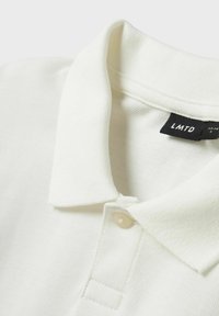 Weißes Polohemd aus strukturiertem Material, mit klassischem Kragen, zwei Knopfleiste und einem schwarzen Etikett mit "LMTD" und Größenangaben.