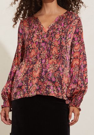 Blouse bunga yang mengalir dalam warna gelap dengan pola merah, pink, dan krim. Memiliki leher V, lengan panjang berbulu, dan potongan santai.