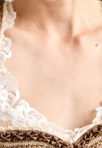 Encolure avec bordure en dentelle superposée sur un tissu marron texturé avec des accents dorés ; des coutures intriquées sont visibles, créant un design détaillé.