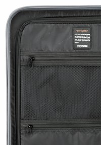 Interno di una valigia nera con un'etichetta, dotato di tasche in rete, cerniere lisce e fodera in tessuto nero. Design pulito e layout funzionale.