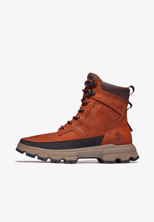 Hnědá kožená bota s vysokým svrškem, černými akcenty a robustní podrážkou. Obsahuje kovové očky a logo na straně. Design na šněrování.