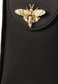 Black textured leather bag featuring a gold bee-shaped clasp as the main accent detail. Clasp showcases intricate wings and body design.